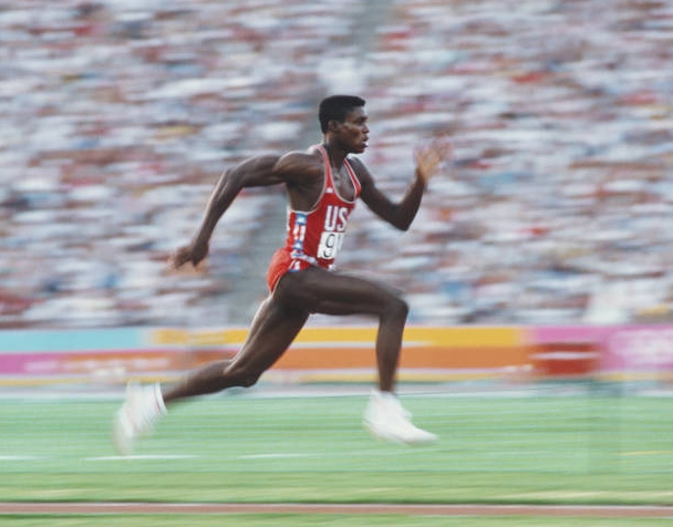 Carl Lewis đang tăng tốc dũng mãnh trên đường chạy đà để thực hiện phần thi nhảy xa của nam tại Thế vận hội Olympic 1984
