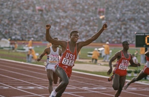 Vận động viên điền kinh người Mỹ Carl Lewis mặc áo đấu Kappa màu đỏ giang tay ăn mừng chiến thắng tại Olympic mùa hè 1984 ở Los Angeles